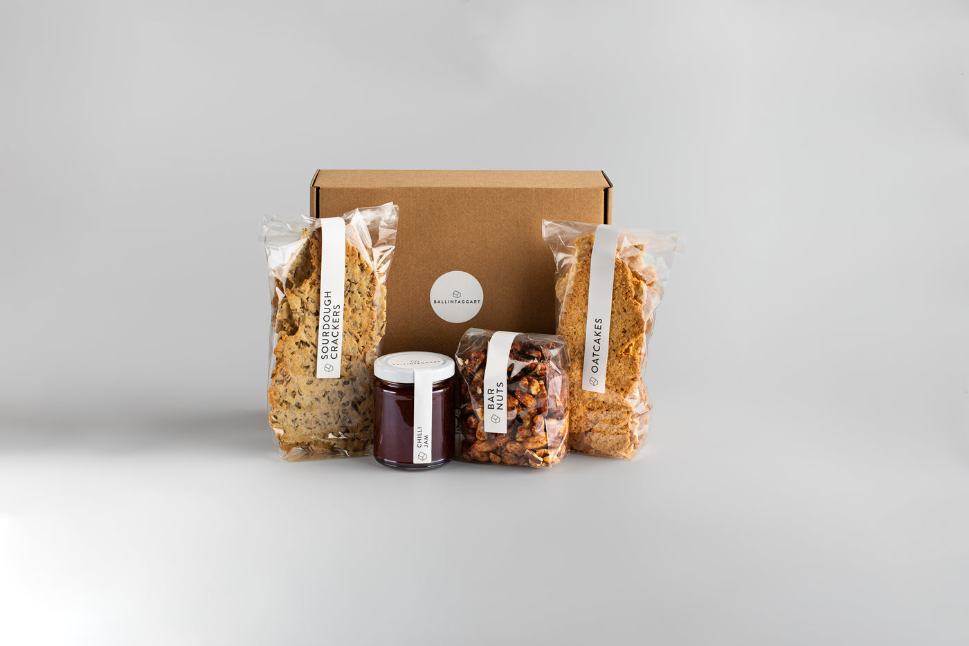 Gourmet food gift set with a cardboard box, granola bags, and jars on a light gray background