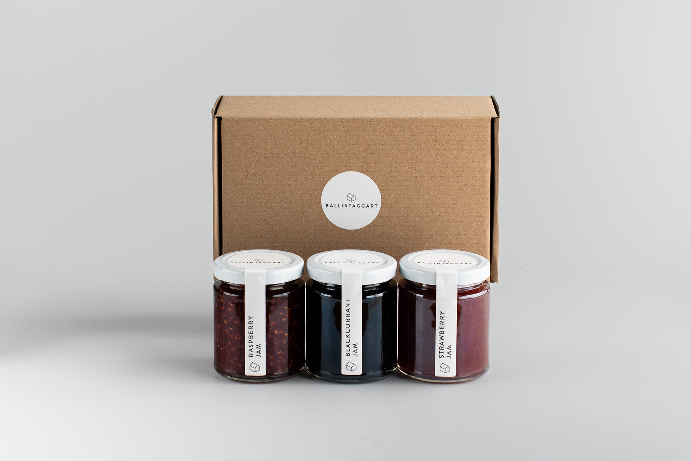 Three jars of jam with a cardboard box on a light gray background