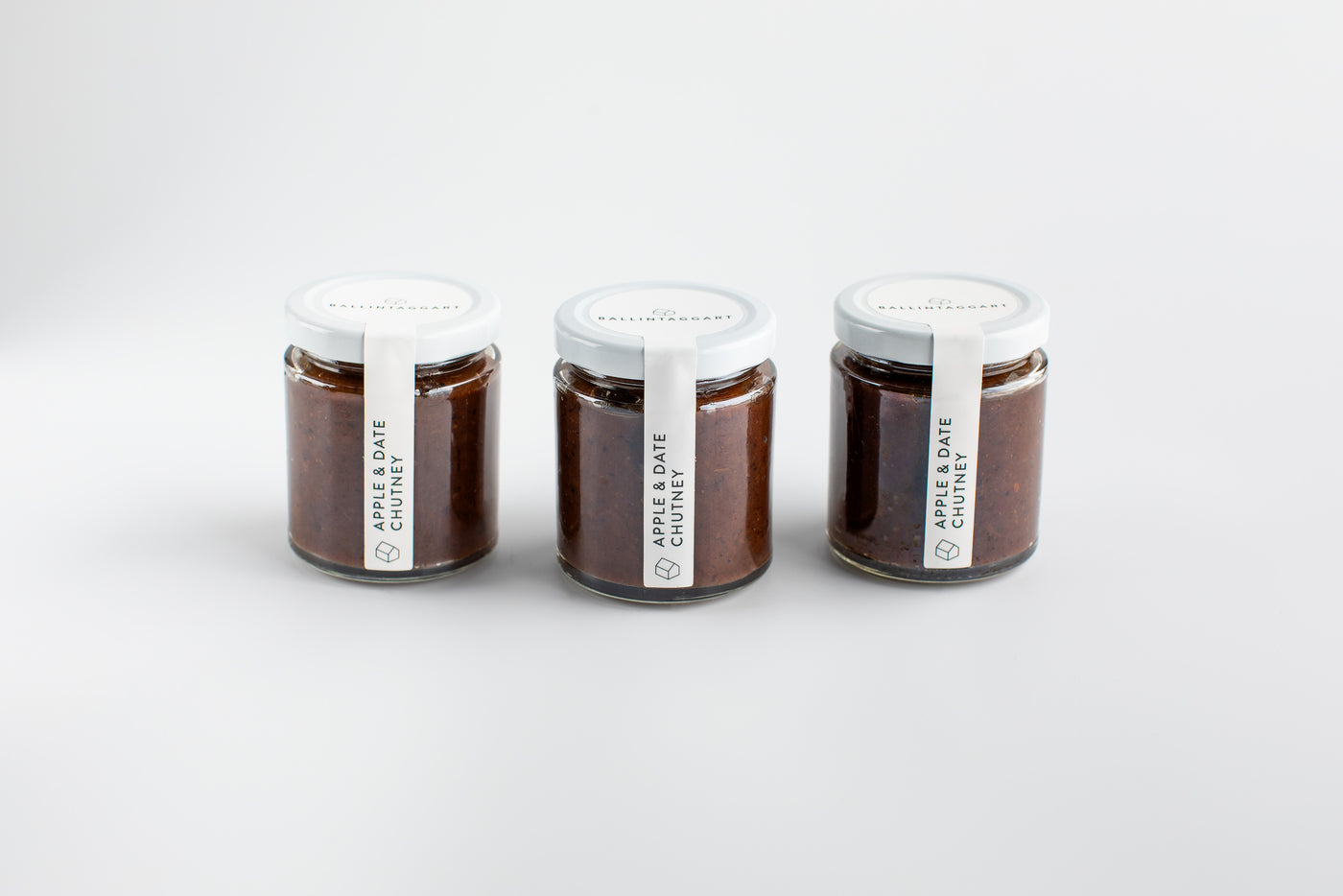 Three jars of apple and date chutney on a white background