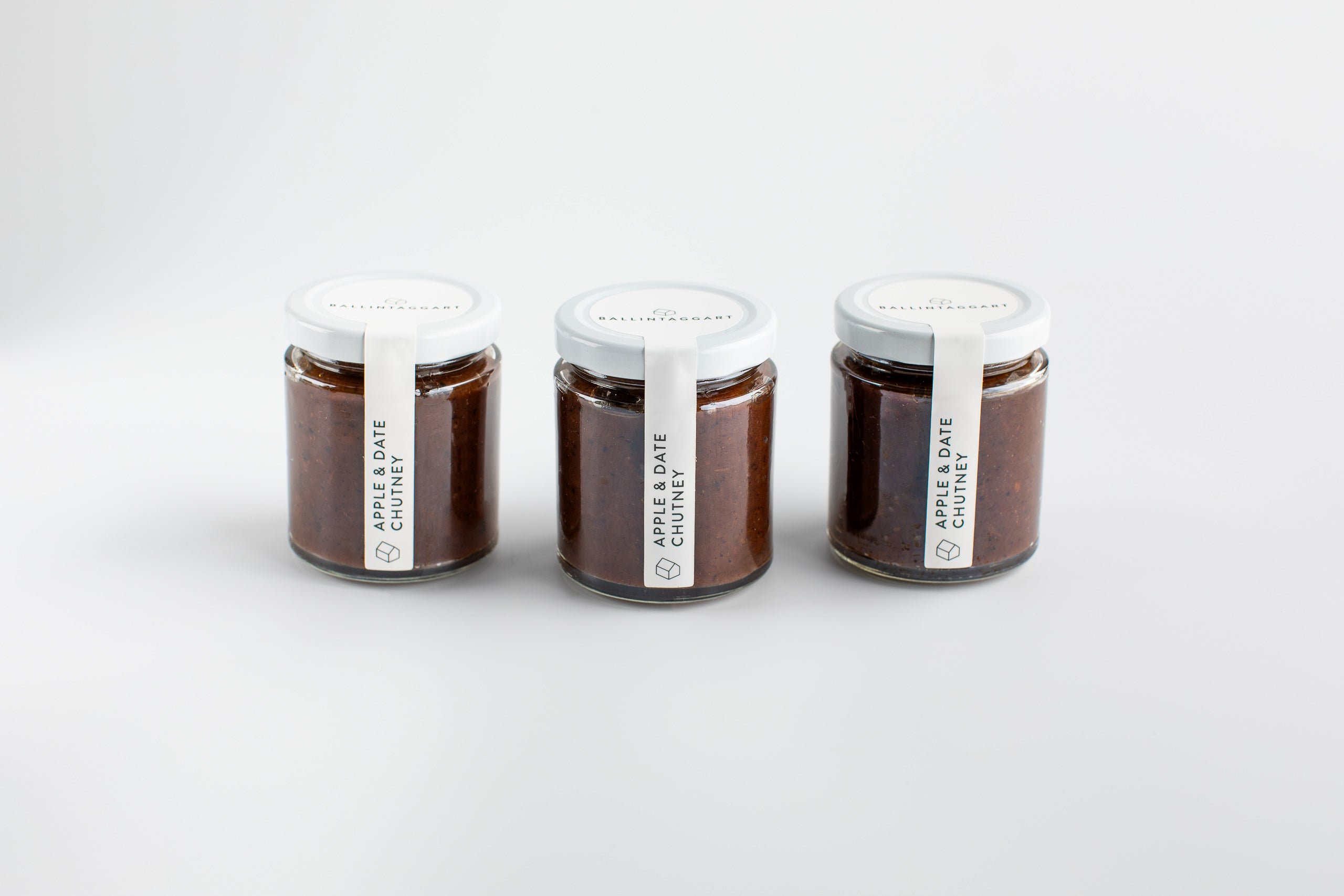Three jars of apple and date chutney on a white background