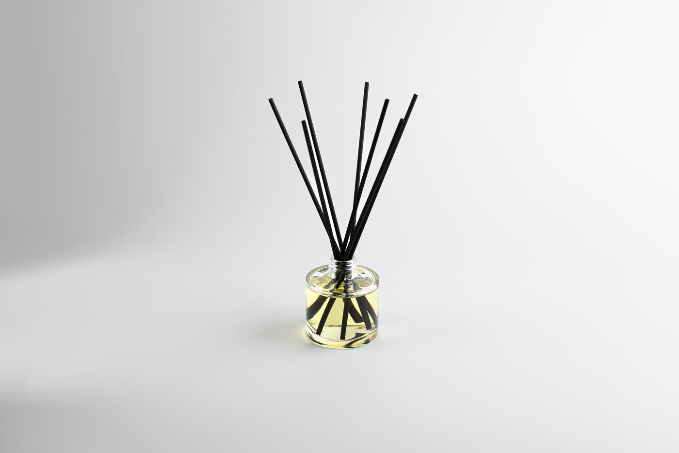 Diffuser with black sticks in a clear container on a light gray background