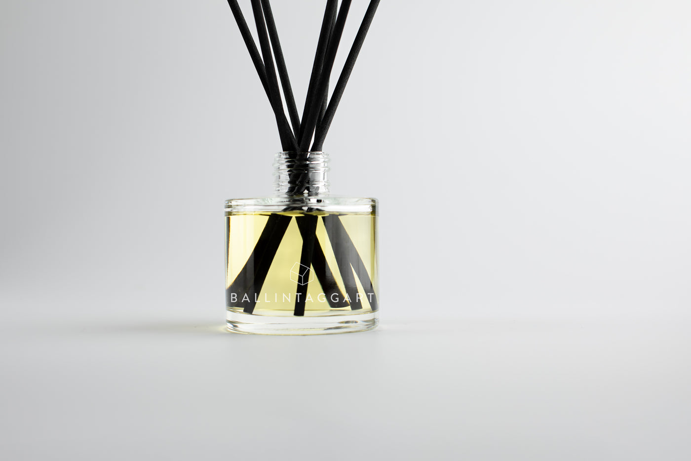Bottle of Ballintagagrt reed diffuser with black sticks on a light gray background