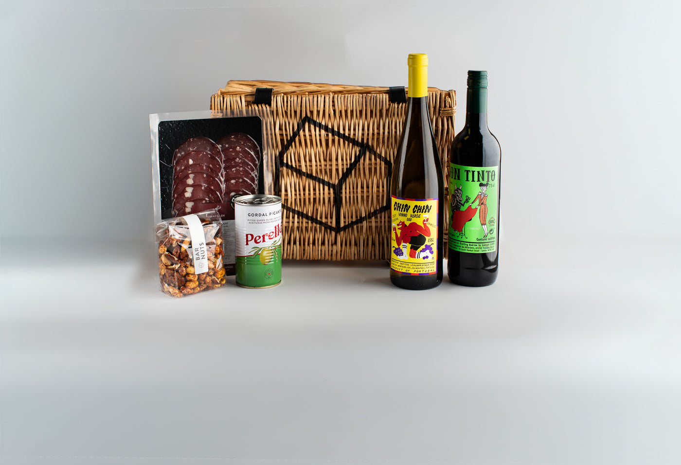 Wicker basket with assorted food items including bottles and a can on a light gray background