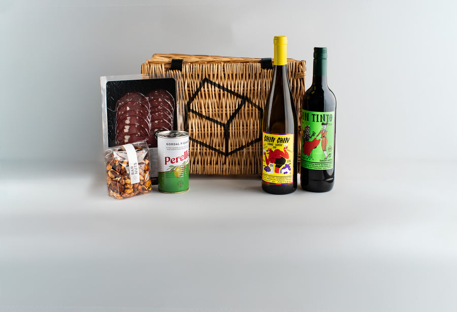 Wicker basket with assorted food items including bottles and a can on a light gray background