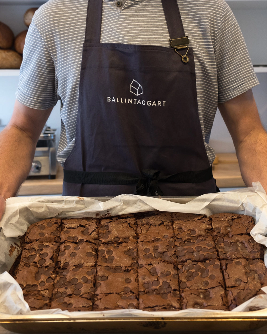 Person wearing a Ballintaggart apron with a tray of brownies in a kitchen setting