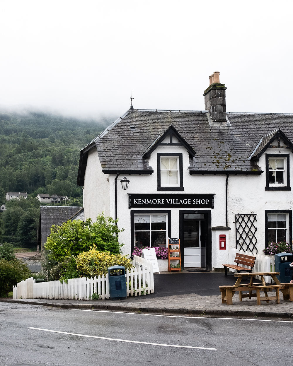White building with 'Kenmore Village Shop' sign on a street corner with greenery in the background