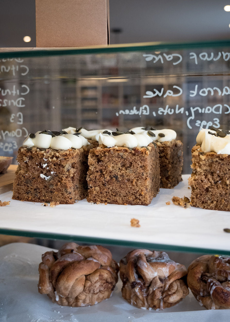 Small square cakes with white frosting and chocolate chips on a glass display case.