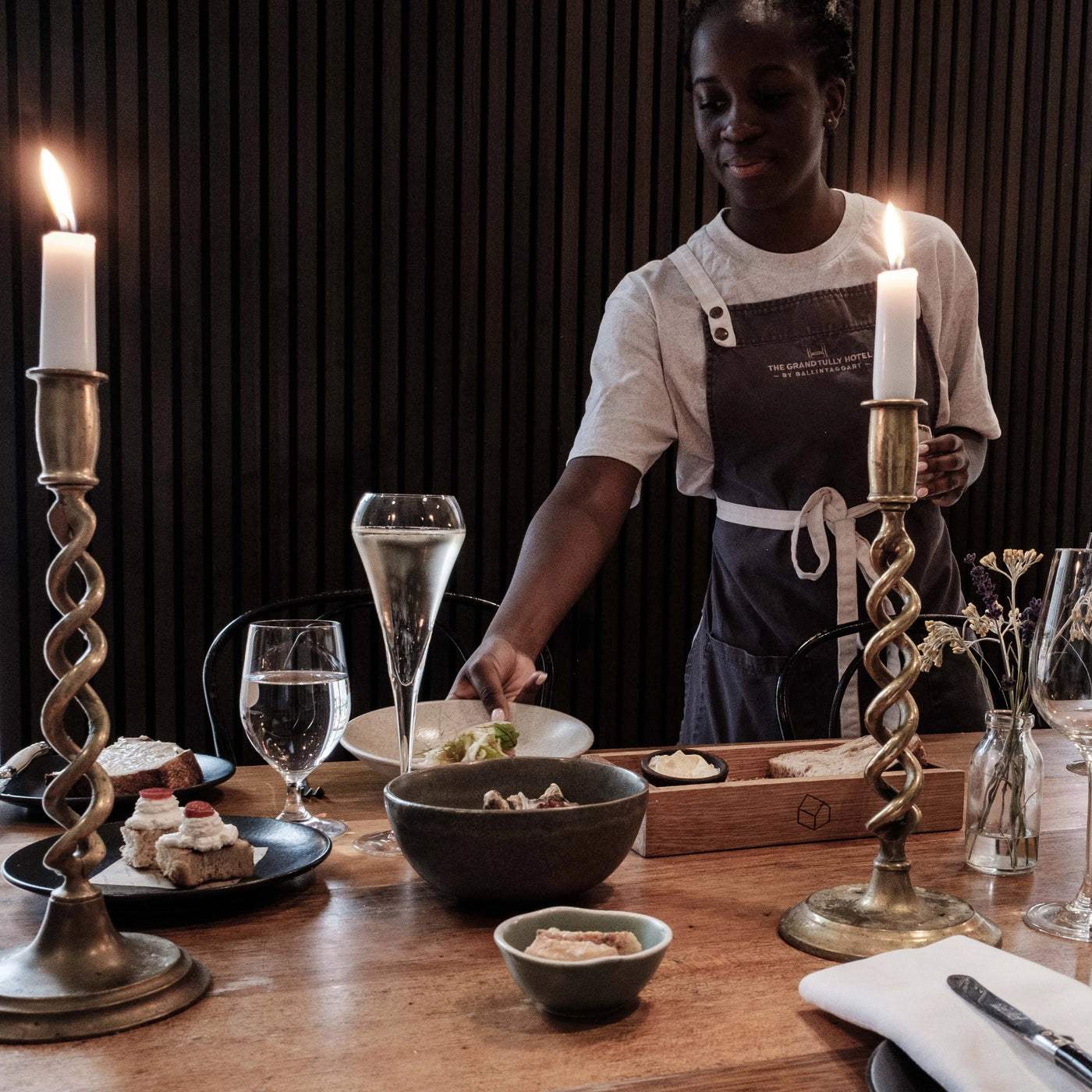 Person setting a table with candles and dishes in a restaurant setting