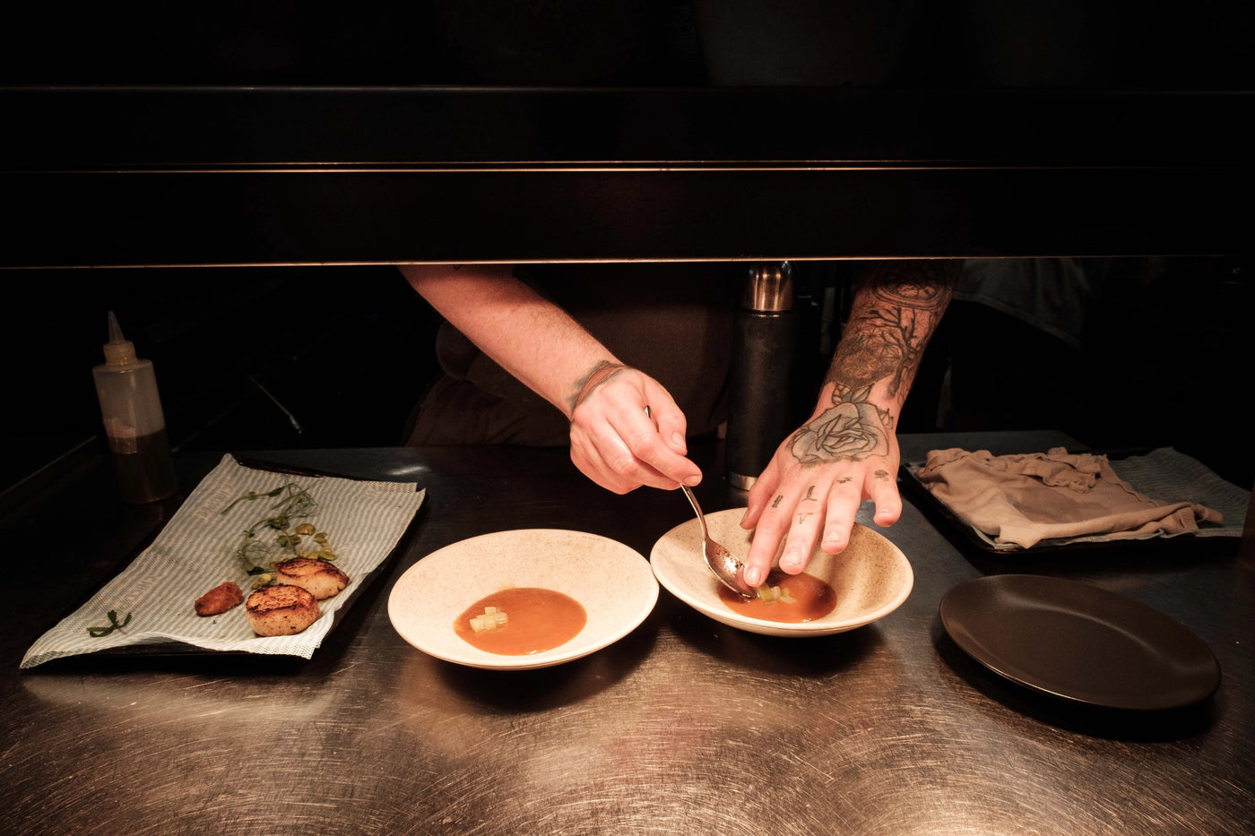 Chef preparing food on a steel table with various dishes and utensils.