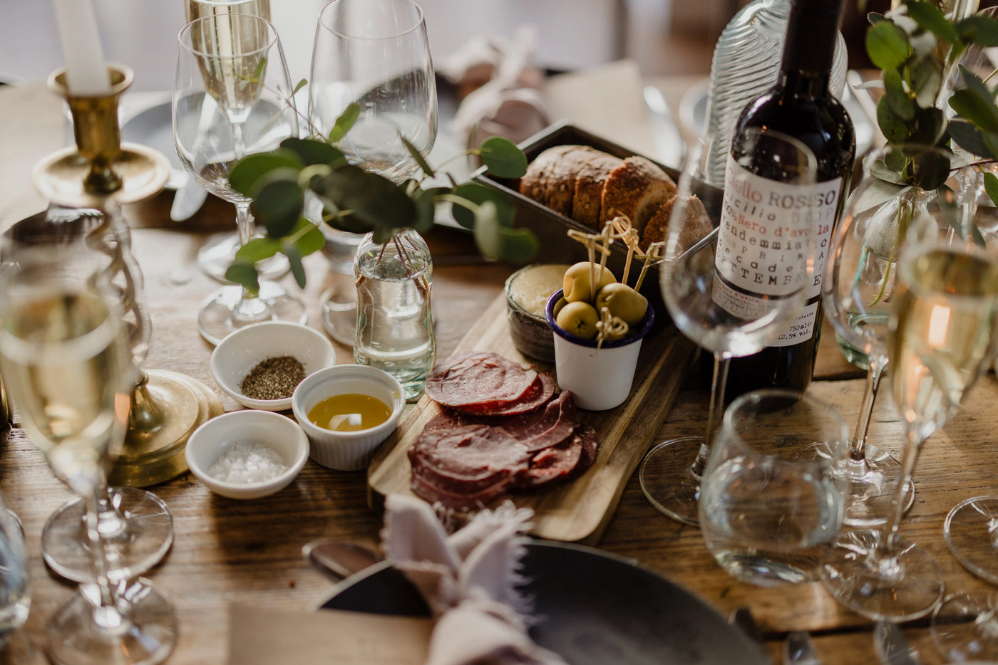Dining table set with wine, appetizers, and glasses on a wooden surface.