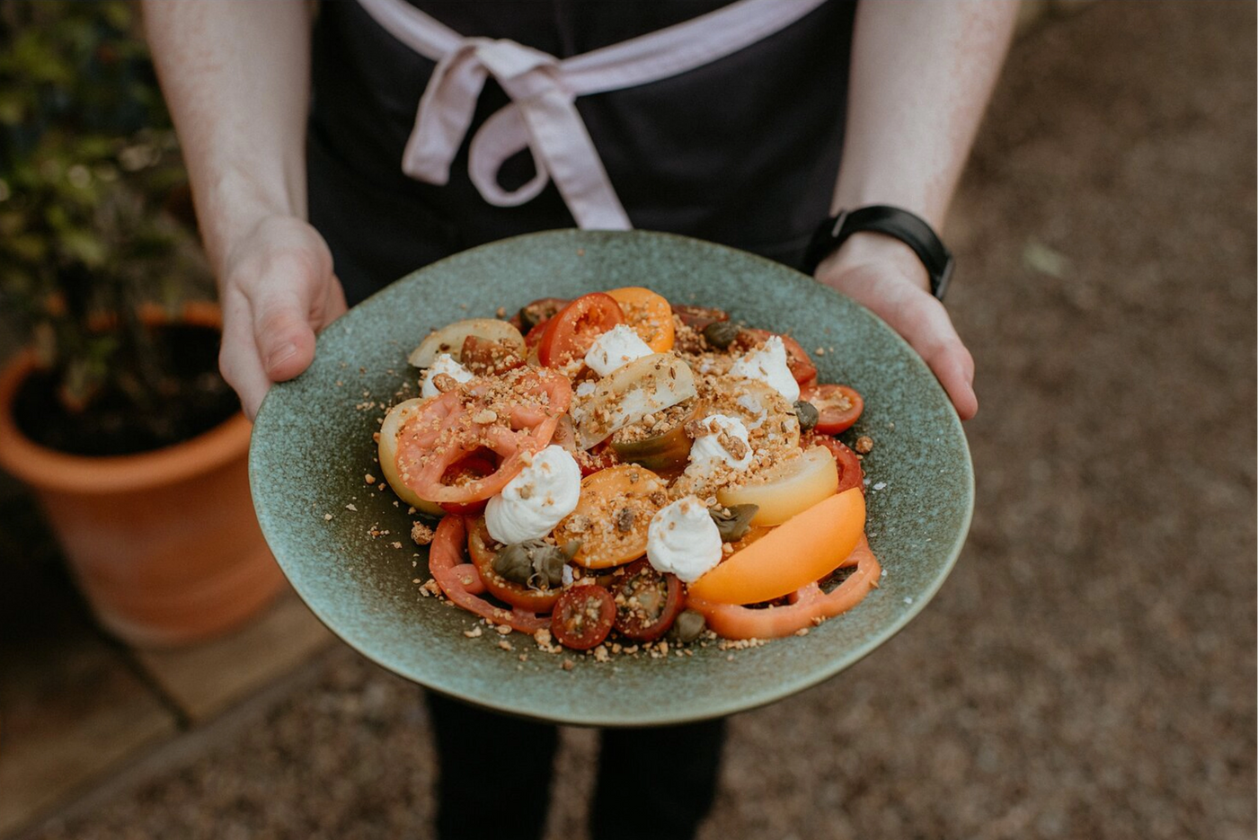 Person holding a plate of salad with tomatoes and feta cheese.