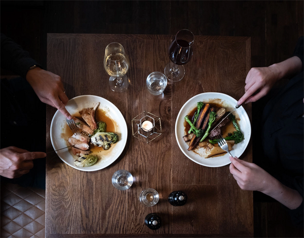 Two people enjoying a meal at a wooden table with plates of food and glasses.