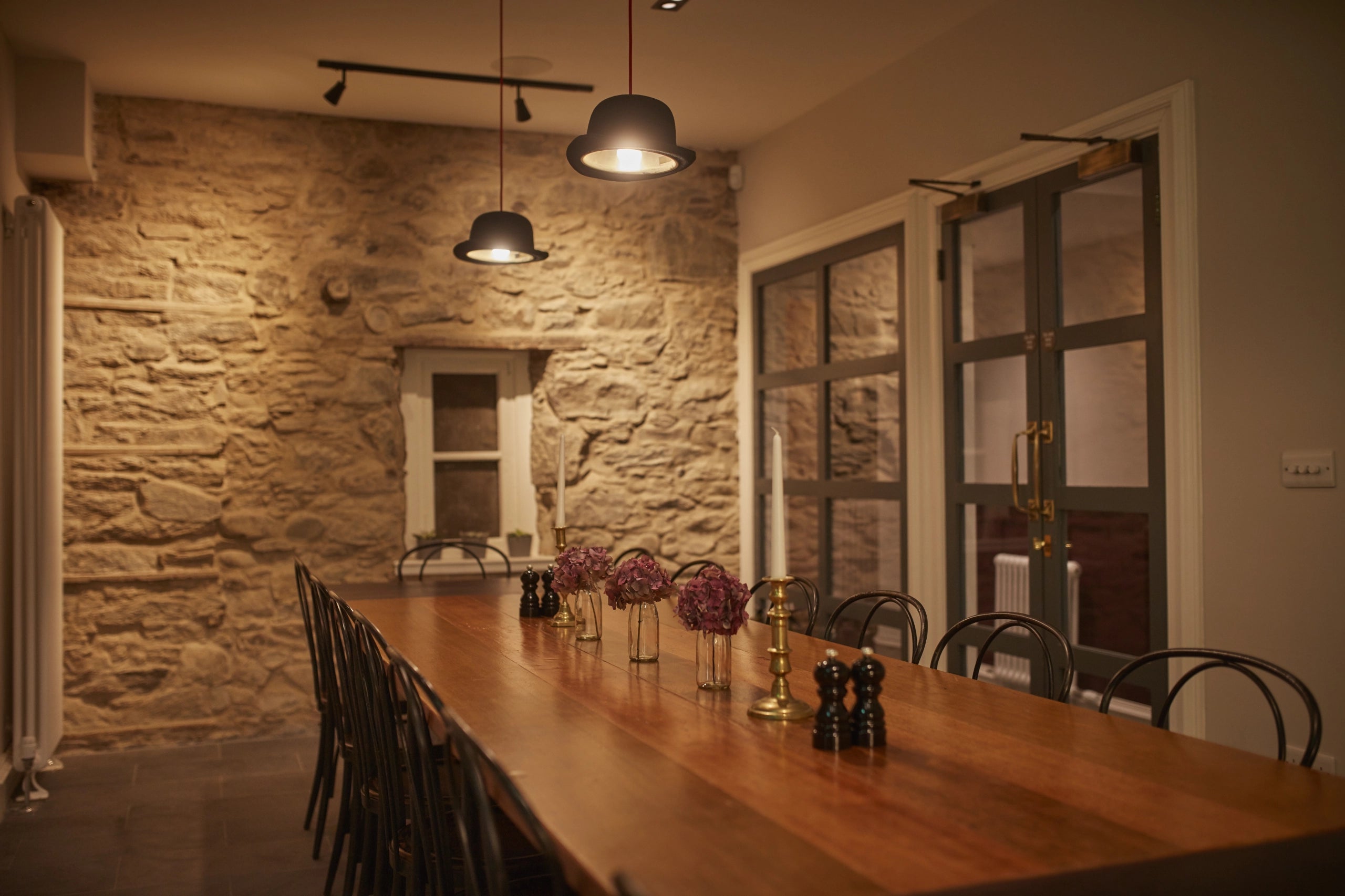 Dining room with wooden table and chairs against a stone wall.