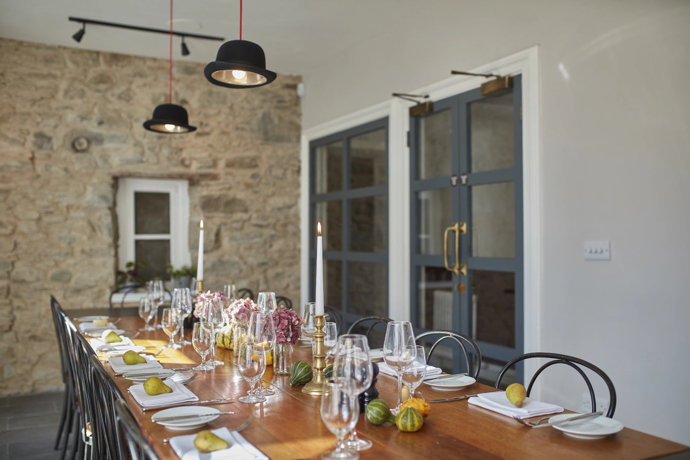 Dining table set for a meal with wine glasses, plates, and candles in a rustic setting.
