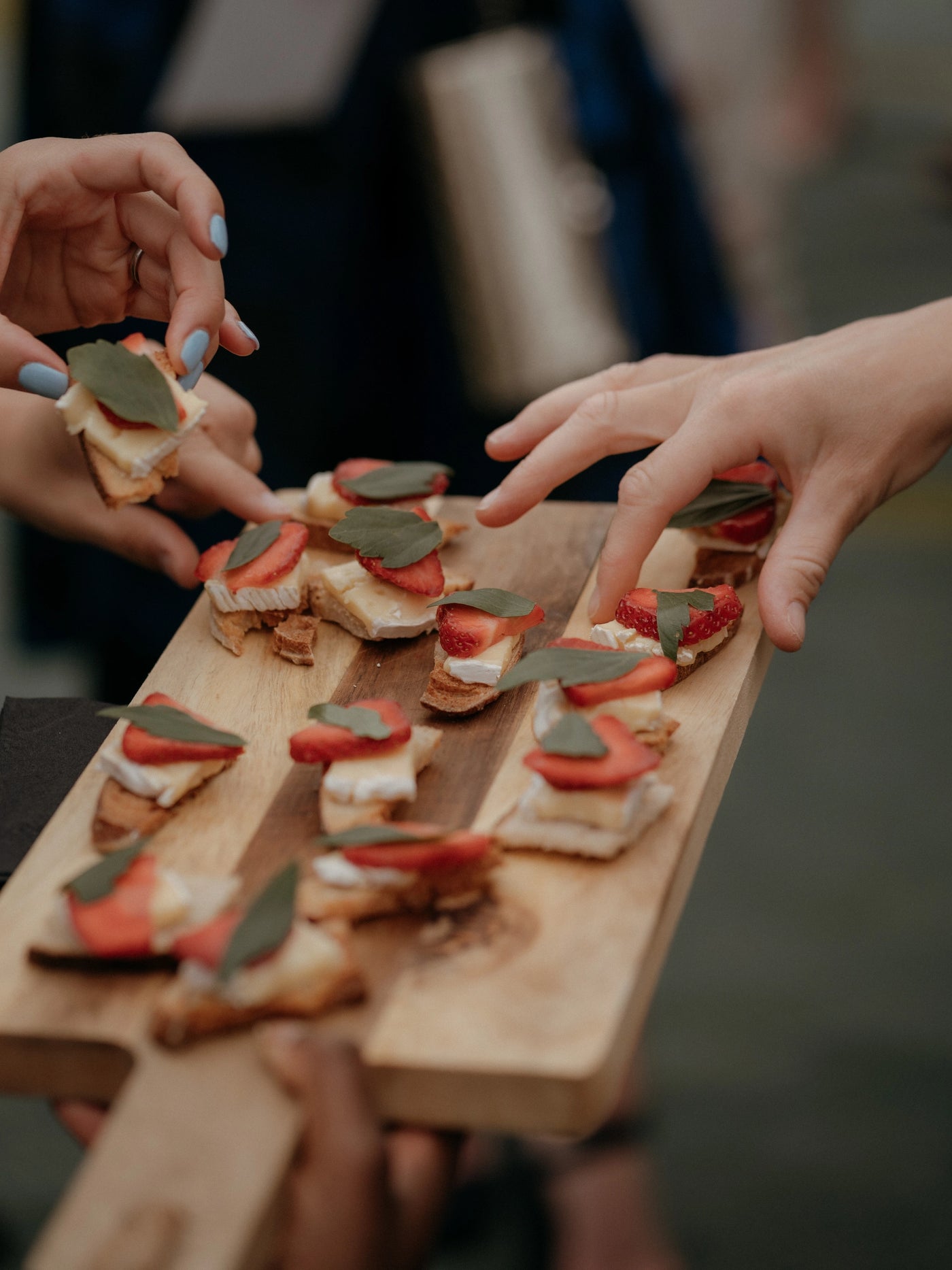 Wooden platter with small appetizers being served to hands
