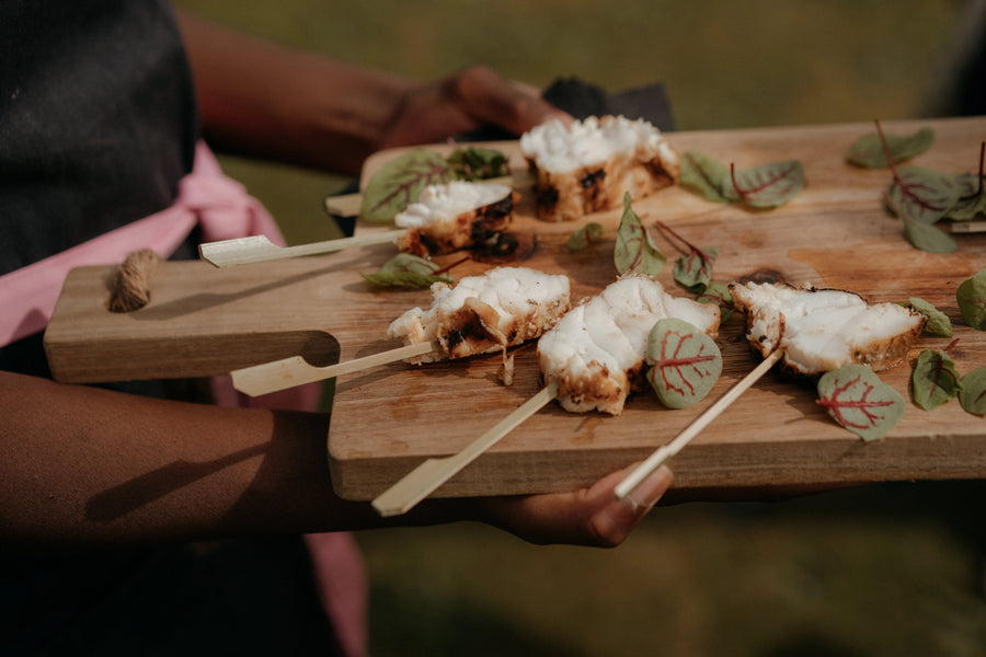 Wooden board with food items on skewers held by a person