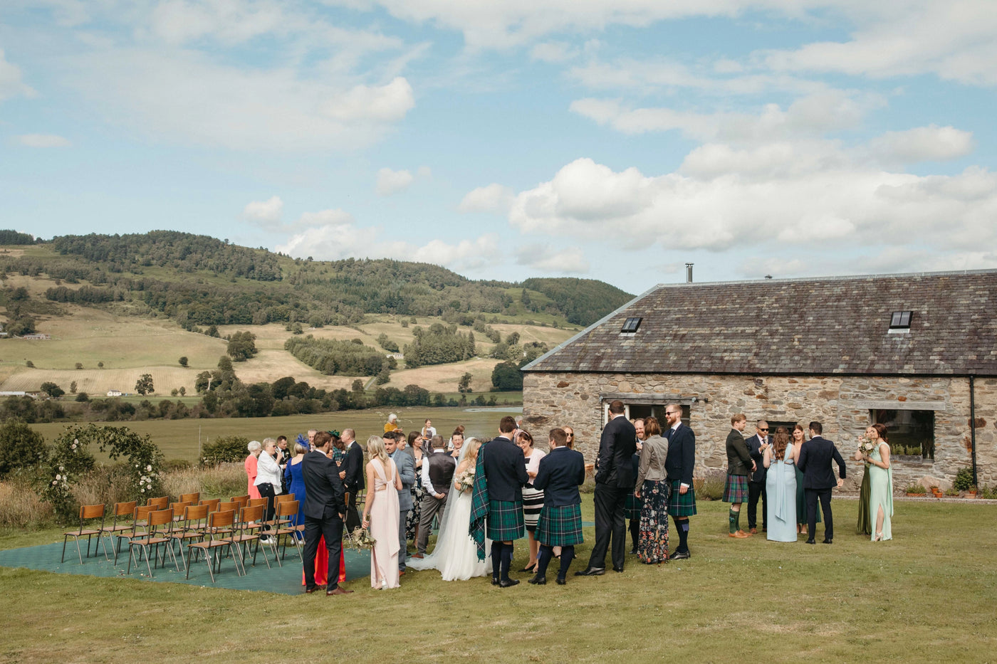 Wedding ceremony outdoors with guests and a stone building in the background