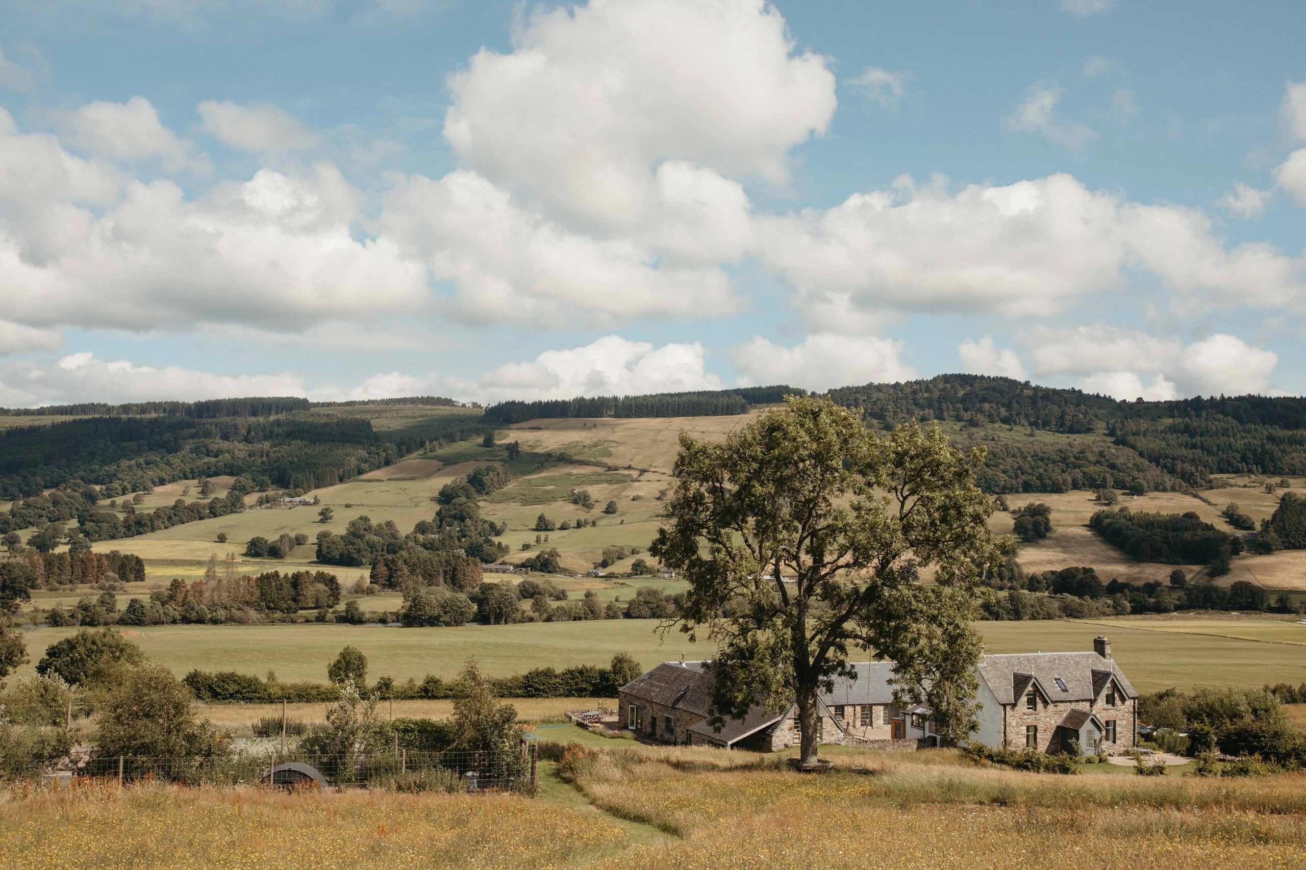 Rural landscape with a house and trees under a blue sky with clouds.