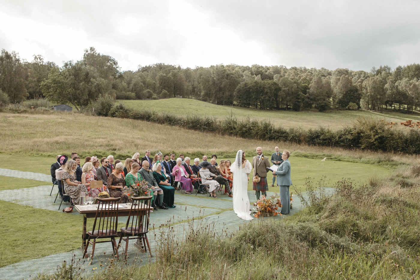 Wedding ceremony outdoors with guests and a couple in a scenic setting.