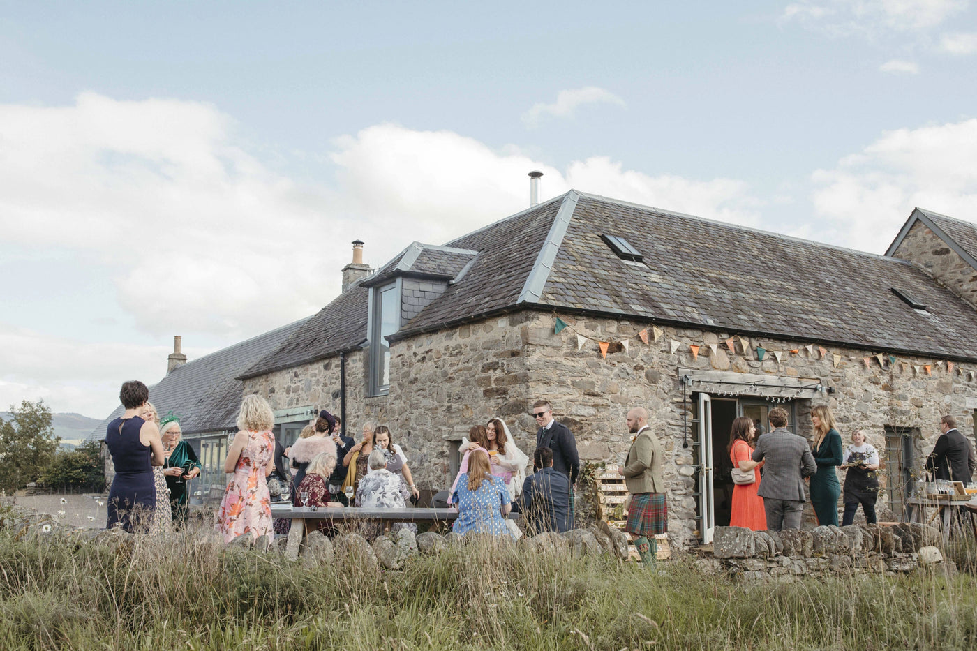 Group of people gathered outside a stone building on a sunny day.