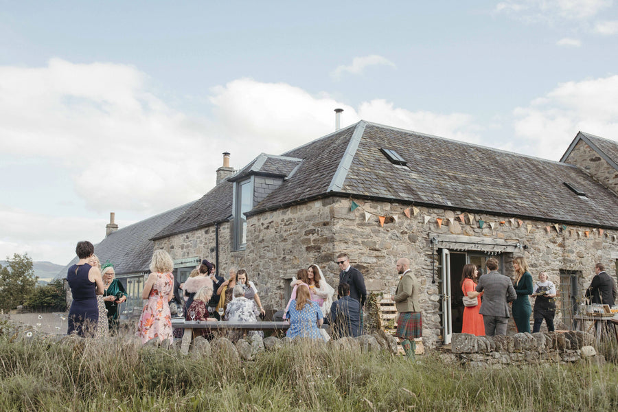 Group of people gathered outside a stone building on a sunny day.