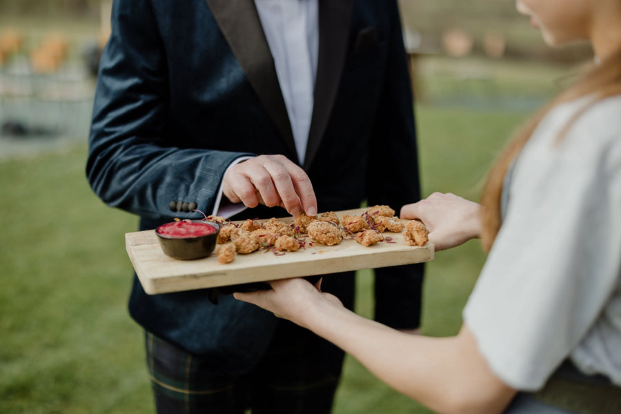 Person offering a platter of food to another person outdoors.